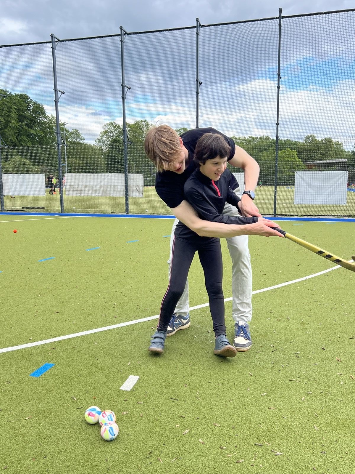 Trainer zeigt einem jungen Teilnehmer Hand in Hand die richtige Technik mit dem Hockeyschläger