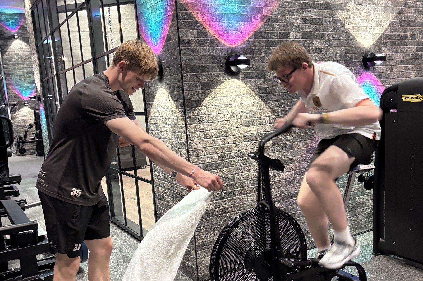 Trainer betreut einen Teilnehmer beim intensiven Training auf dem Airbike im Gym