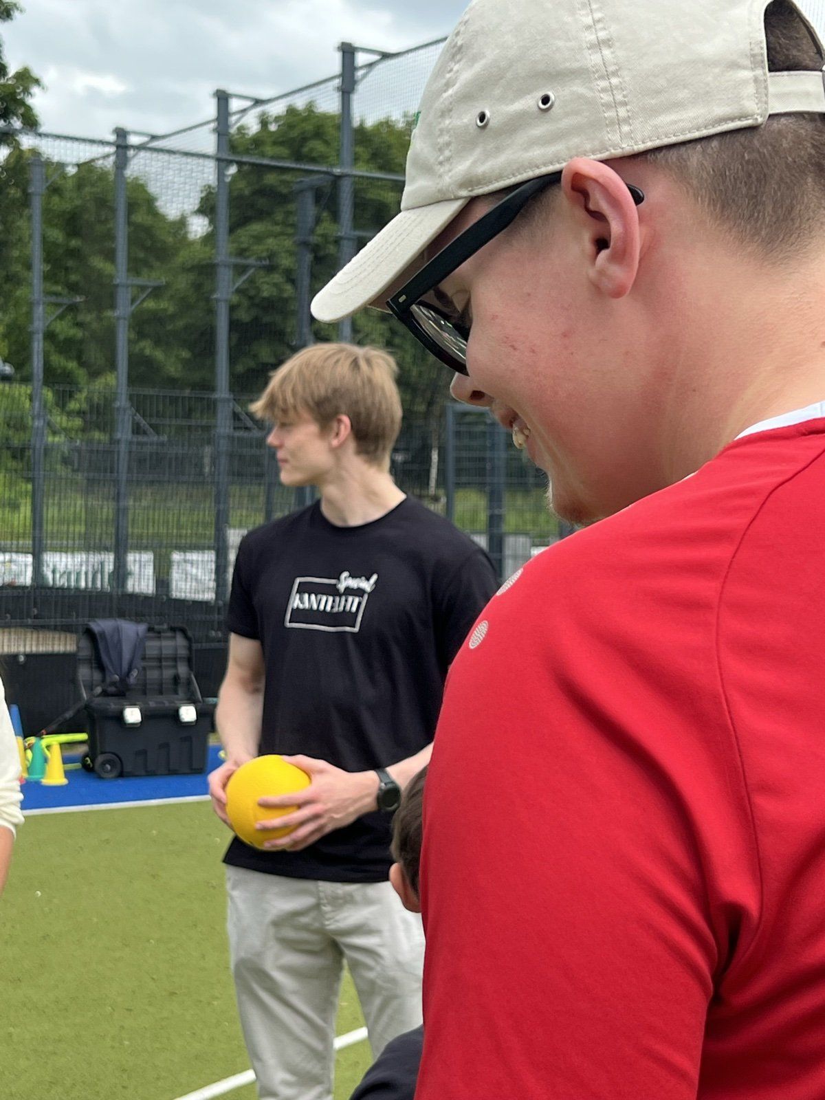 Trainer und Teilnehmer lachen zusammen, ein gelber Ball in der Hand