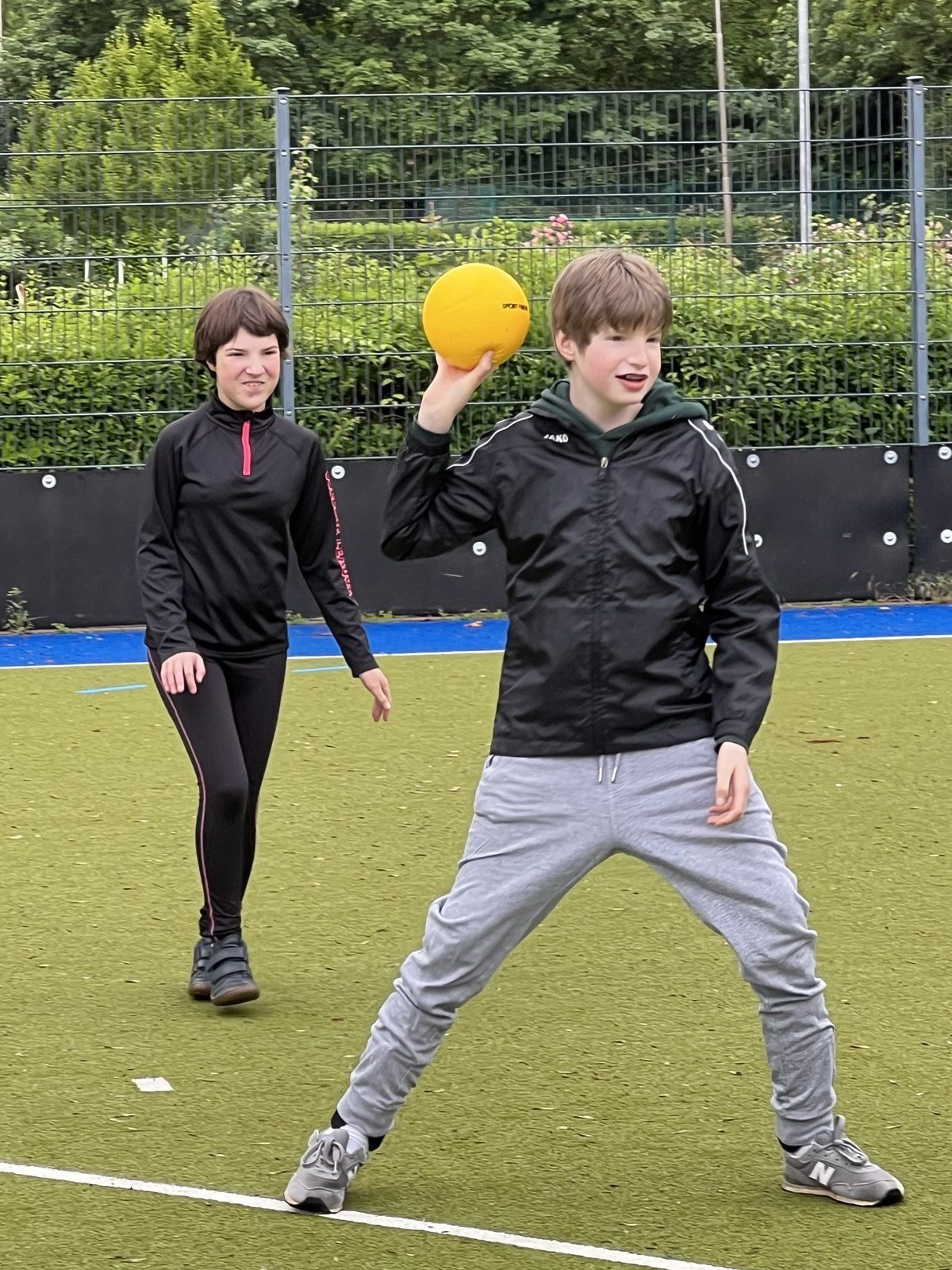 Junger Teilnehmer wirft einen gelben Ball, Trainerin begleitet die Übung