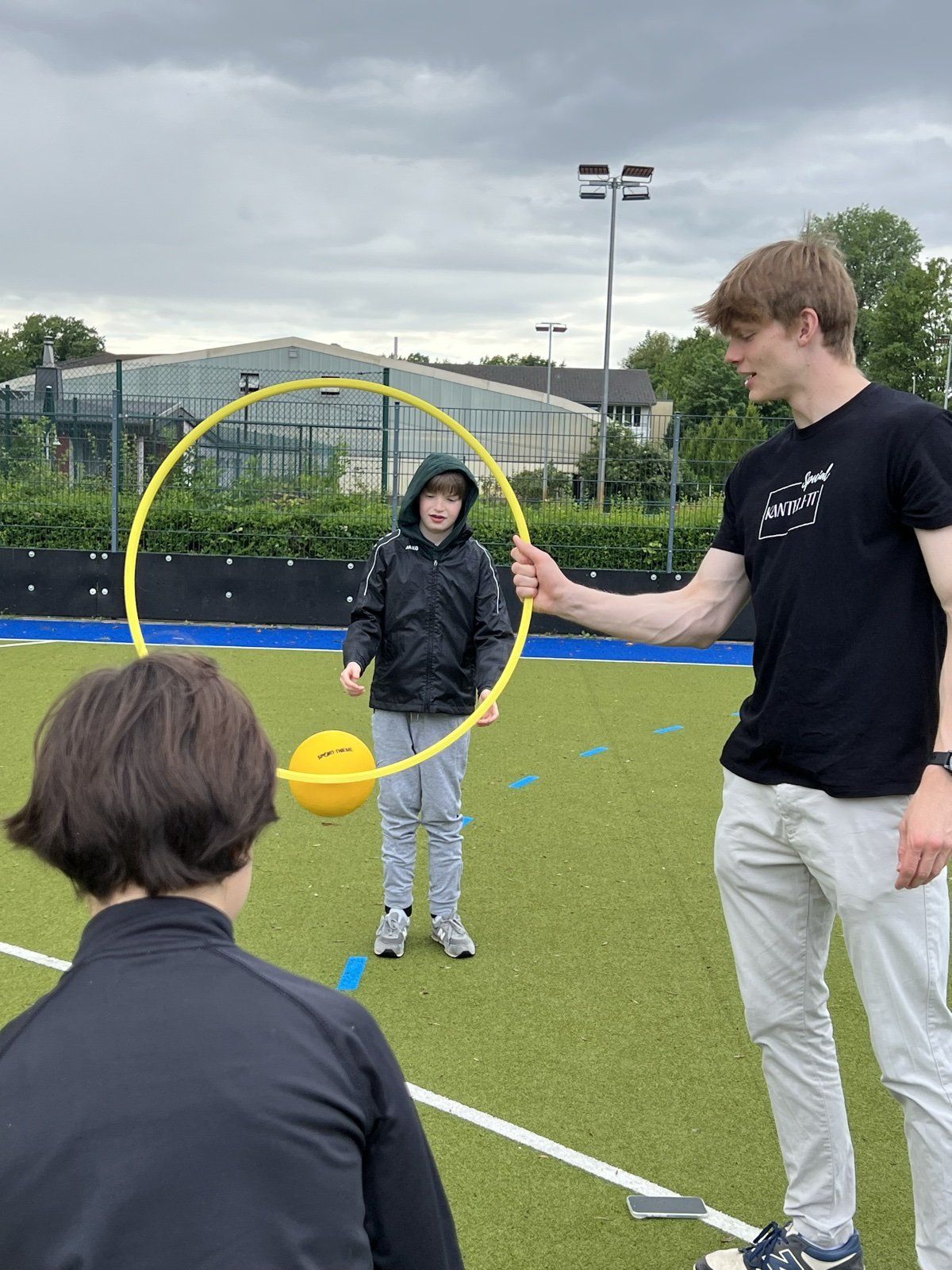 Trainer hält einen gelben Reifen, durch den ein Teilnehmer einen Ball wirft