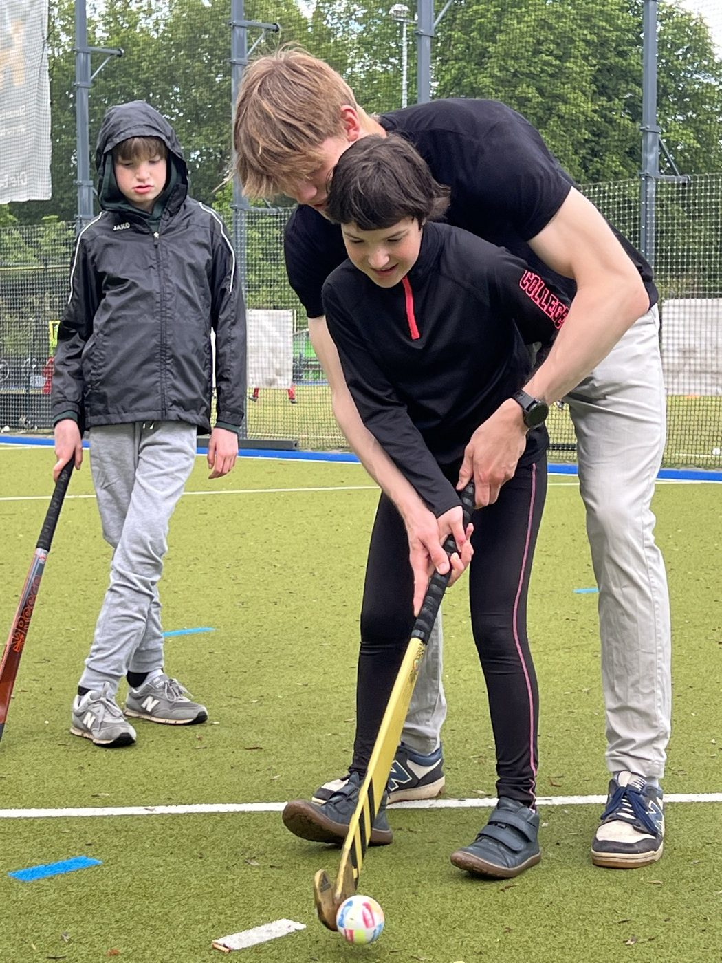 Trainer führt einen Teilnehmer Hand in Hand durch eine Hockey-Übung