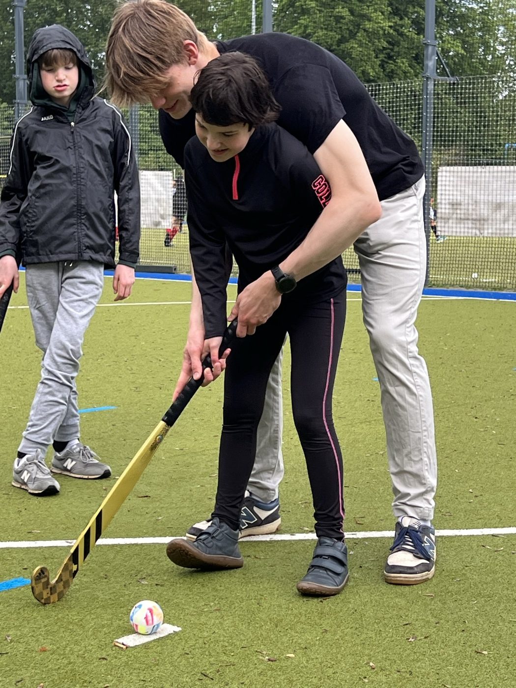 Trainer führt die Hände einer Spielerin am Hockeyschläger